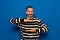 Positive bearded man in striped pullover holding something invisible in his hands next to his abdomen and smiling at