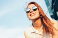 Positive beautiful happy red haired girl in mirror sunglasses on blue sky background, summer sunset time Royalty Free Stock Photo