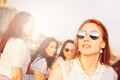 Positive beautiful happy red haired girl in the mirror sunglasses with friends on blue sky background, summer sunset time Royalty Free Stock Photo