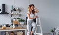 Positive beautiful young woman on a white wooden stepladder on the background of a stylish modern kitchen. Royalty Free Stock Photo