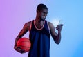 Positive black basketball fan watching championship online, cheering for his favorite team on smartphone in neon light