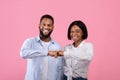 Positive black couple bumping fists, celebrating achievement or success, reaching common goal on pink studio background