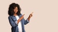 Positive black woman pointing at copy space on grey