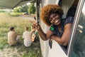 Positive Black female owner of traveling camper looking out of the vehicle's window, smiling at camera, and pointing