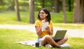 Positive black girl with laptop studying online at green summer park, empty space Royalty Free Stock Photo