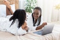 Positive black girlfriends lying on bed at home, using laptop