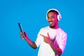 Positive black guy pointing at digital tablet, using headphones Royalty Free Stock Photo