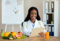 Positive black nutritionist with clipboard creating healthy meal plan for patient at clinic, blank space