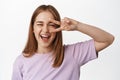 Positive blond girl, winking and smiling, showing v-sign positive peace gesture, living carefree life, enjoying summer Royalty Free Stock Photo