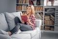 A girl sits on a couch and reads a book in a living room. Royalty Free Stock Photo