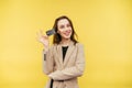 Positive business woman in a jacket stands on a yellow background with a plastic bank card in hand and looks at the camera with a Royalty Free Stock Photo