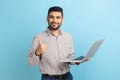 Positive businessman standing with portable computer in hand, looking at display, showing thumb up. Royalty Free Stock Photo