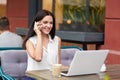 Positive businesswoman in formal clothes, has telephone conversaton, speaks with colleague, uses laptop computer for making busine Royalty Free Stock Photo