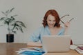 Positive busy woman with European appearance works on freelance digital project, earns money online on distance job, sits at