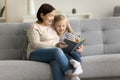 Positive grandma reading book to granddaughter kid on comfortable couch