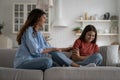 Positive caring woman wants to cheer up introverted teenage girl sits on couch in closed shy pose