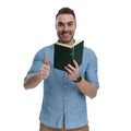 Positive casual holding book and giving thumbs up, smiling