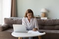 Positive Caucasian millennial woman doing domestic paperwork at home