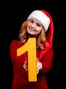 Smiling pretty girl in a christmas hat holding number 1 on a black background. New year 2018 concept. Royalty Free Stock Photo