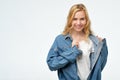 Positive cheeky caucasian blonde girl in jeans jacket smiling at camera