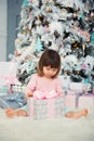 Positive cheerful baby girl sitting with Christmas gift near Christmas tree. Happy New Year Royalty Free Stock Photo