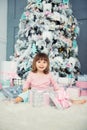 Positive cheerful baby girl sitting with Christmas gift near Christmas tree. Happy New Year Royalty Free Stock Photo