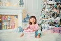 Positive cheerful baby girl sitting with Christmas gift near Christmas tree. Happy New Year Royalty Free Stock Photo