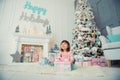Positive cheerful baby girl sitting with Christmas gift near Christmas tree. Happy New Year Royalty Free Stock Photo