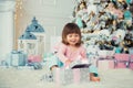 Positive cheerful baby girl sitting with Christmas gift near Christmas tree. Happy New Year Royalty Free Stock Photo