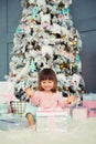 Positive cheerful baby girl sitting with Christmas gift near Christmas tree. Happy New Year Royalty Free Stock Photo