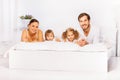 Positive cheerful family laying on white bed