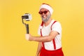 Positive cheerful man in santa claus costume and stylish sunglasses posing on camera of smartphone in his hand, blogger recording Royalty Free Stock Photo