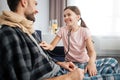 Positive and cheerful picture of small girl using stethoscope. She smiles to dad. Guy look at her. He covered in blanket Royalty Free Stock Photo