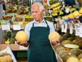 Positive senior male owner of greengrocery shop in apron offering fresh fruits and vegetables Royalty Free Stock Photo