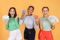 Positive three multiethnic young ladies holding cash and credit card