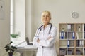 Positive confident elderly woman doctor in uniform standing and looking at camera Royalty Free Stock Photo
