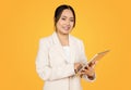 Positive confident korean millennial woman in suit typing on tablet, chatting