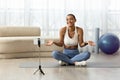 Positive confused millennial latin lady blogger in sportswear sit on floor, shooting video fitness blog