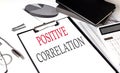 POSITIVE CORRELATION text on paper clipboard with chart and notebook on withe background