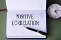 POSITIVE CORRELATION - words in a white notebook on a dark green background with a clock