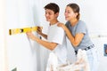 Positive couple checking laid tiles on wall with level meter in room under renovation