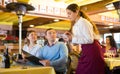 Positive couple consulting with young waitress while making order in restaurant Royalty Free Stock Photo