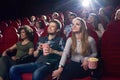 Positive couple watching funny movie at cinema and eating popcorn.