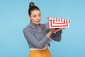 Positive curious nosy woman with hair bun in denim jacket unpacking and opening small carton box, looking inside with interest