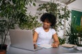 Portrait of curly African-American young woman in headphones writing notes, watching webinar, studying online using Royalty Free Stock Photo