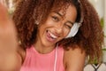 Positive curly Afro American girl blinks eyes, shows tongue, being in good mood, hears melody in headphones, stretches