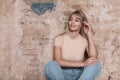 Positive cute young blond woman in stylish clothes posing near a vintage brick wall indoors. Beautiful funny girl fashion model Royalty Free Stock Photo