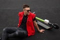 Positive cute young man in fashionable clothes in sunglasses sits and smiles near an electric scooter on the street. Happy hipster Royalty Free Stock Photo