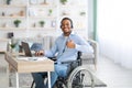 Positive disabled black man in headset using laptop computer for online work, showing thumb up gesture at home