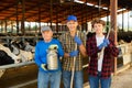 Positive elderly cow breeder with adult son and teenage grandson in cowshed